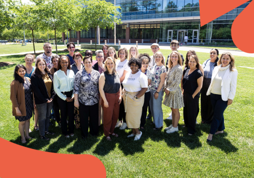 A group of people standing together in a grassy field in front of a glass building.