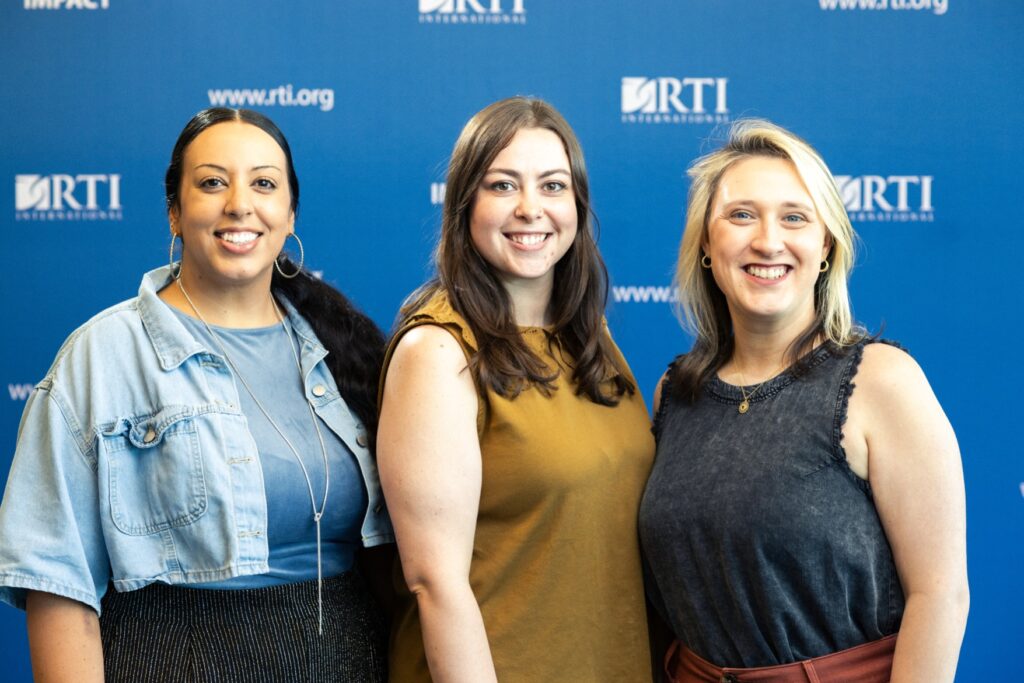 Three women standing together in front of a blue background.